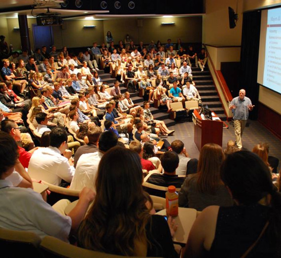 A woman in graduation cap and gown holds up her degree and smiles